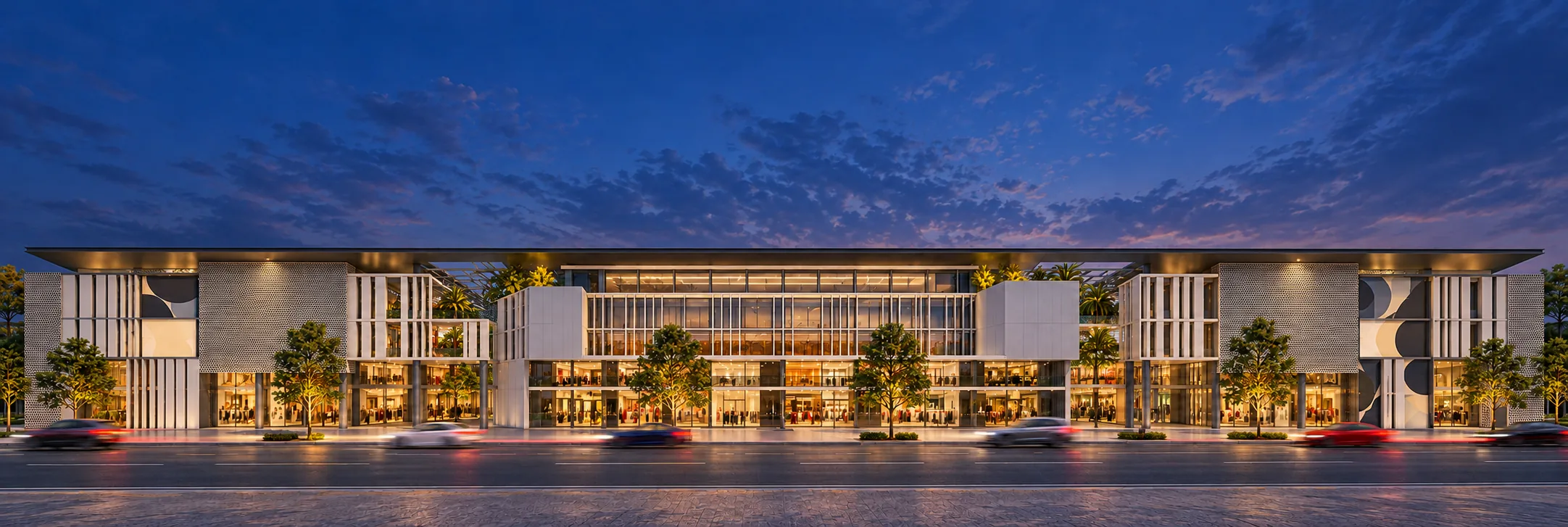 Panorama of a long low-rise commercial building with a flat roof canopy, perforated panels and glass shopfronts behind a tree-lined street